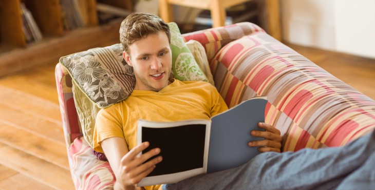 Young man reading magazine on his couch at home in the living room