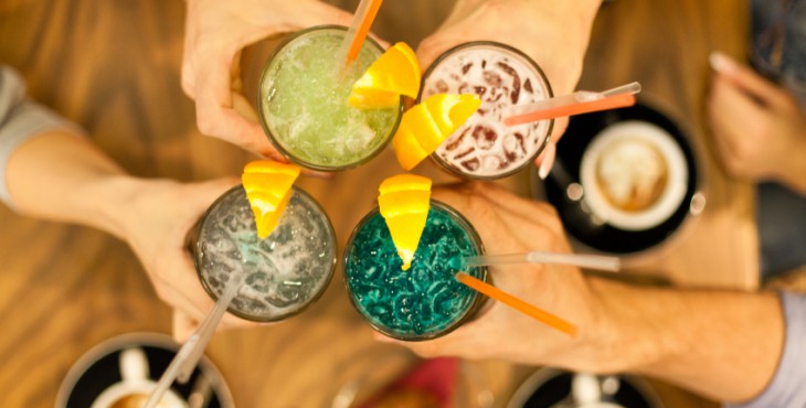 Friends toasting with colorful drinks in a cafe