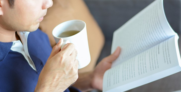 A man reading book with hot tea cup in another hand