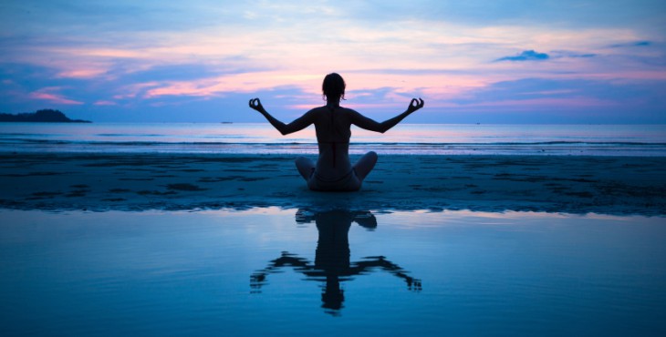 Woman practicing yoga on the beach at sunset (with reflection in water)