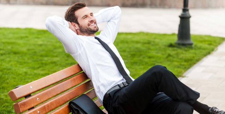 Enjoying green spaces in his city. Top view of happy young businessman keeping eyes closed and holding hands behind head while sitting on the bench outdoors